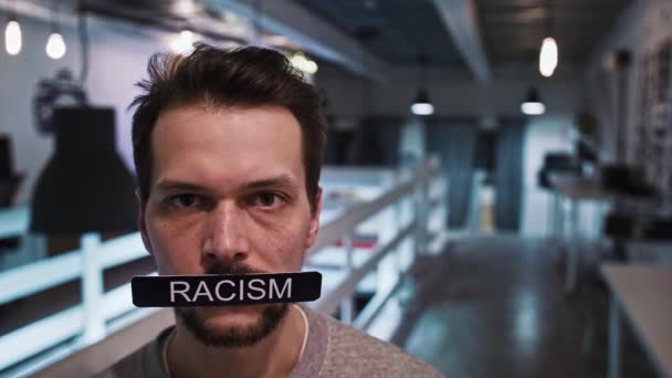 El hombre mira a la cámara y sostiene un cartel en su boca que dice RACISMO - Metraje, vídeo