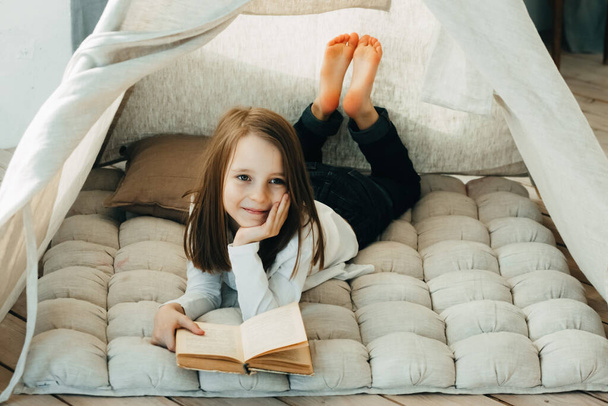 A lány otthon olvas egy könyvet egy gyerekkunyhóban, házi feladat a kovid-19 alatt. - Fotó, kép