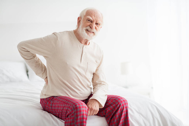 Photo of senior man unhappy sad upset hand on spine ache pain spasm disorder sit on bad home rest healthcare - Foto, Imagen