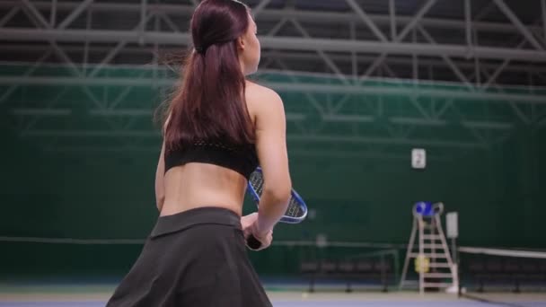 junge Tennisspielerin spielt auf Indoor-Court, schlägt Ball mit Tennisschläger, läuft über Fläche - Filmmaterial, Video