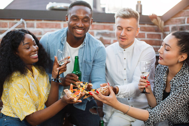 Four friends enjoying pizza and alcoholic drinks on party - Zdjęcie, obraz