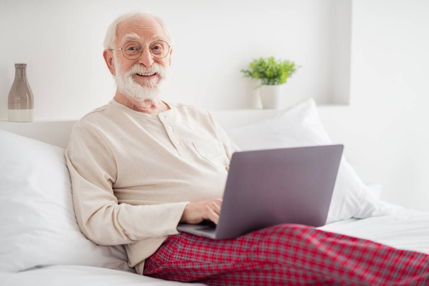 Photo of elderly man happy positive smile sit bed house wear pajamas chat type email browse internet laptop - Fotoğraf, Görsel