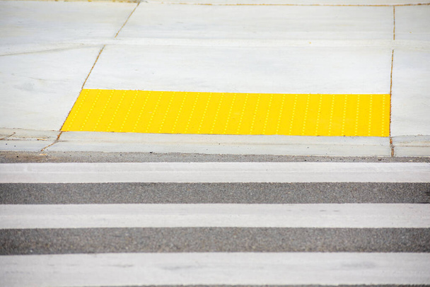 Πεζόδρομος που διασχίζει οδηγεί σε κίτρινο ανιχνεύσιμη επιφάνεια προειδοποίησης απτική πλακόστρωση. Επιλεκτική εστίαση - Φωτογραφία, εικόνα
