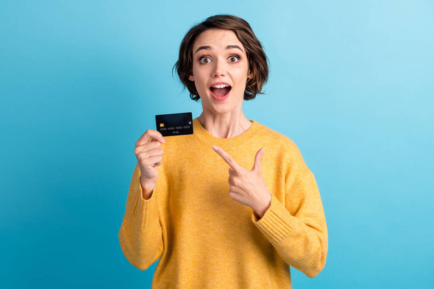 Portrait of cute surprised young brunette short hairstyle lady point on card wear yellow sweater isolated on bright blue color background - Foto, Imagem