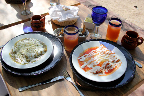 tyylikäs meksikolainen aamiainen, hedelmämehu ja vihreä ja punainen enchiladas ulkona pöydällä - Valokuva, kuva
