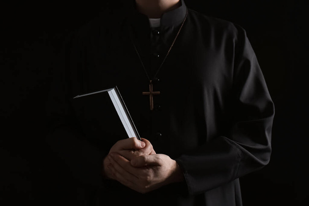 Priest with Bible on dark background, closeup - Foto, afbeelding