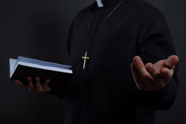 Priest in cassock with Bible on black background, closeup - Фото, зображення