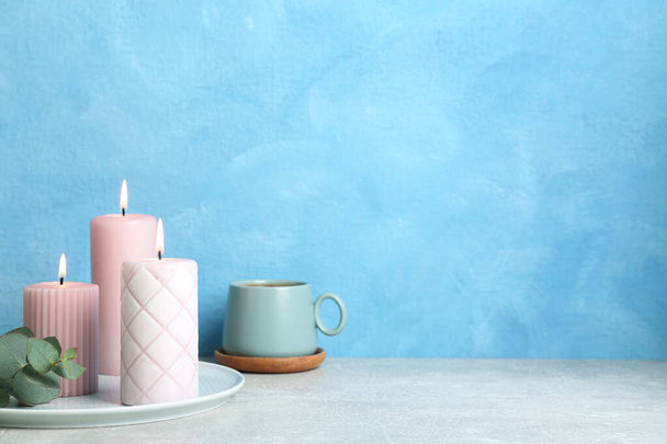 Scented candles, eucalyptus and cup on grey table near light blue wall, space for text - Valokuva, kuva