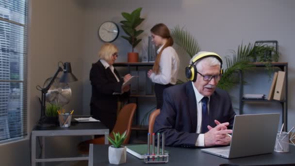 Fröhlicher älterer Geschäftsmann, der am tragbaren Laptop am Schreibtisch sitzt, Musik hört und tanzt - Filmmaterial, Video