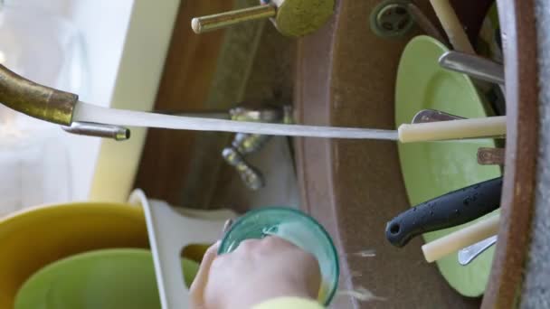 Tiro vertical Ama de casa lava una taza de vidrio sucio en el fregadero con una esponja con detergente. - Imágenes, Vídeo