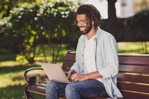 Photo portrait of man in glasses working on computer doing project sitting on bench in park smiling - Photo, Image