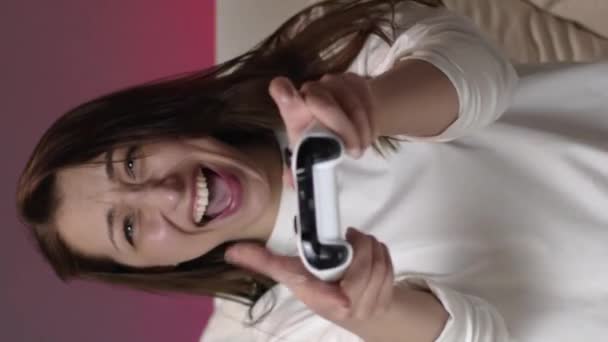 Verticaal schot Vreugdevolle aantrekkelijke vrouw in witte pyjama speelt video games met joystick in bed - Video
