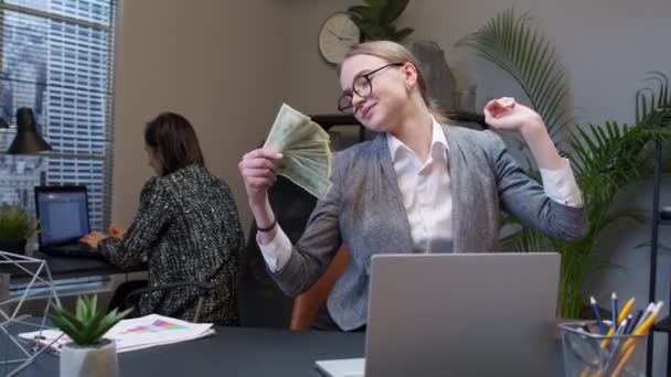 Χαμογελώντας νεαρή επιχειρηματίας κυματίζει με στοίβα των χρημάτων δολάρια μετρητά στο γραφείο στο χώρο εργασίας - Πλάνα, βίντεο