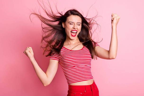 Photo of young beautiful excited happy crazy girl raise fists in victory with flying hair isolated on pink color background - Photo, Image