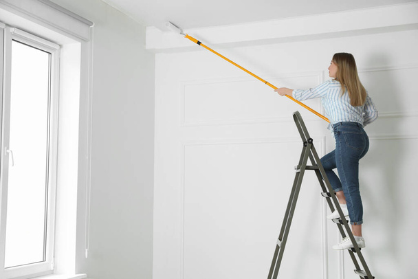 Young woman painting ceiling with white dye indoors, space for text - Foto, Imagem