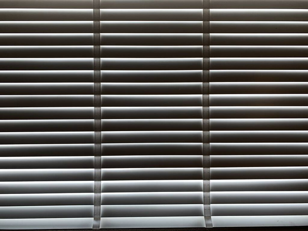 Closeup white color wooden blinds . Sunlight through the windows in the city with garden.Selective focus and light image backdrop. - Photo, Image