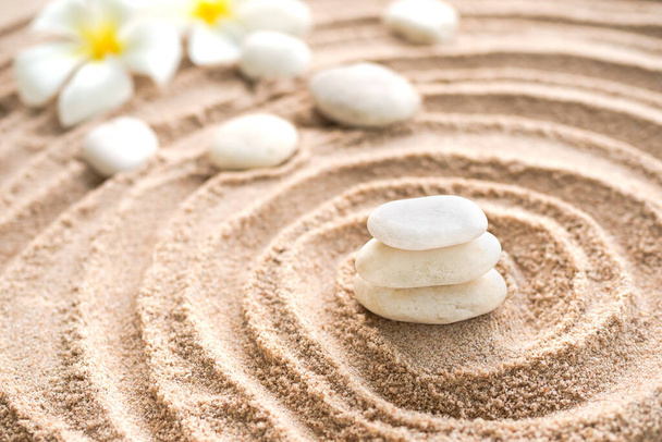 Ιαπωνική πέτρα κήπου zen στην παραλία άμμο. βράχος ή βότσαλο με λουλούδια πλουμέρια με αντιγραφικό χώρο. για σπα αρωματοθεραπείας στις καλοκαιρινές διακοπές. διαλογισμός ευεξία και ηρεμία Ιαπωνική έννοια. - Φωτογραφία, εικόνα