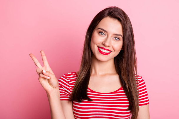 Portrait of young attractive smiling good mood positive girl with red lipstick showing v-sign isolated on pink color background - Photo, Image