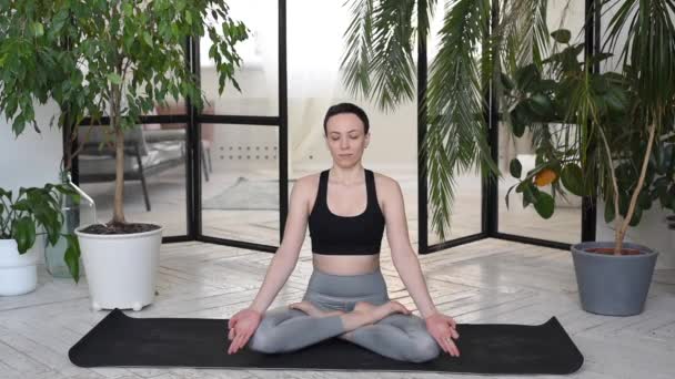 Young woman meditating indoors. Woman sitting in the lotus position. Relaxation and meditation at home near the plants - Imágenes, Vídeo