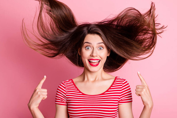Portrait of young attractive excited crazy smiling girl point finger at flying hairstyle isolated on pink color background - Photo, image