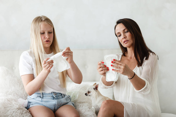 Woman hygene concept. Periods. Menstrual cycle. Mother explains daughter how to use hygiene pads and tampons. Woman and teenage girl talking at home. - Fotoğraf, Görsel