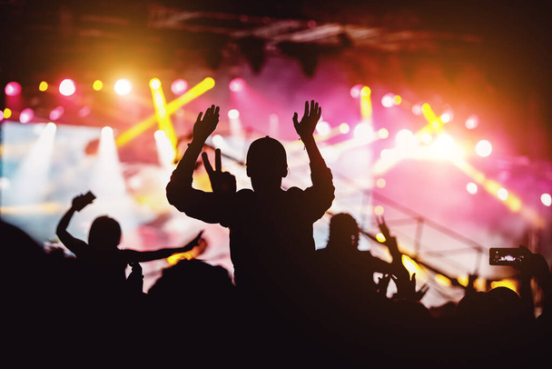 Люди з піднятими руками, силуети концертного натовпу перед яскравими сценічними вогнями
. - Фото, зображення