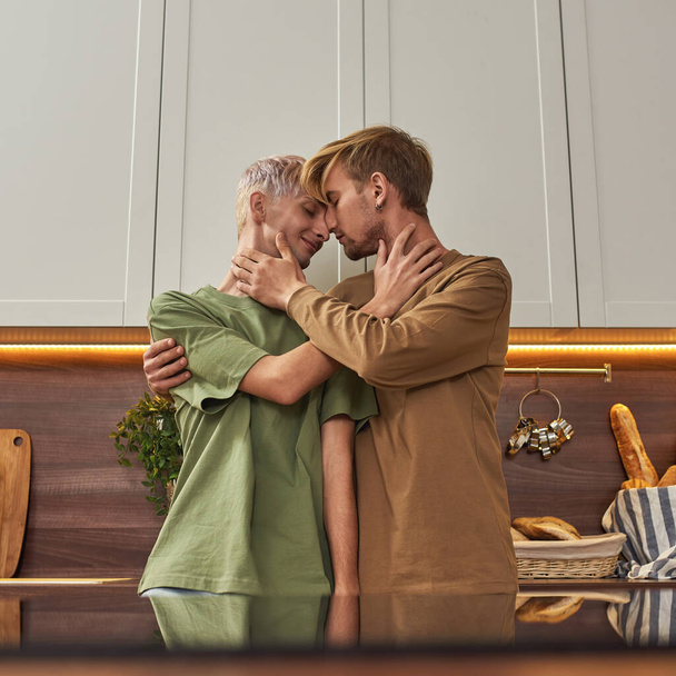 Cheerful homosexual male pair hugging on kitchen - 写真・画像