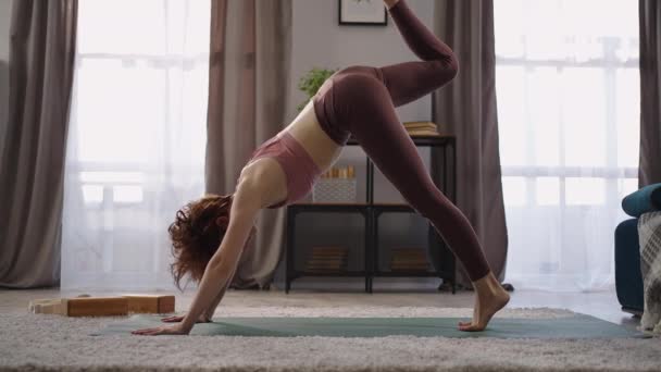 aptidão em casa de mulher treinada, senhora esportiva está realizando asanas de ioga na sala de estar, de pé em pose de cão virada para baixo - Filmagem, Vídeo