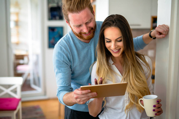 Happy romantic couple using tablet and drinking coffee at home - Foto, afbeelding
