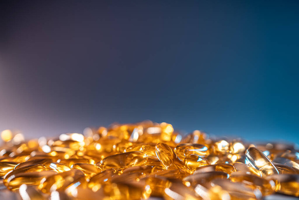 handful of golden fish oil capsules omega 3 vitamins on blue background - Fotografie, Obrázek