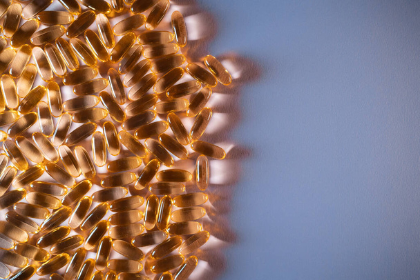 handful of golden fish oil capsules omega 3 vitamins on purple background - Fotografie, Obrázek