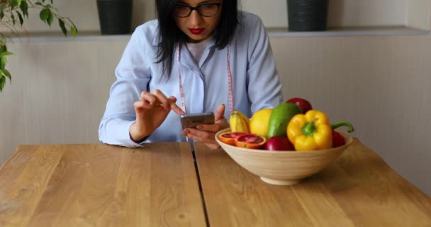 Nutritionist woman with healthy fruit and vegetable using smartphone, Right nutrition and diet concept, Female dietitian with fruits working at her desk at home. - Metraje, vídeo