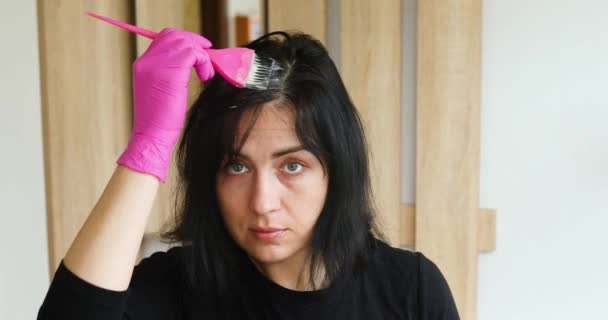 Nuori nainen vaaleanpunainen käsineet soveltamalla maali ruskeaverikkö hiukset itse, kun katsot peiliä kotona. karanteeni, sepelvaltimovirus - Materiaali, video