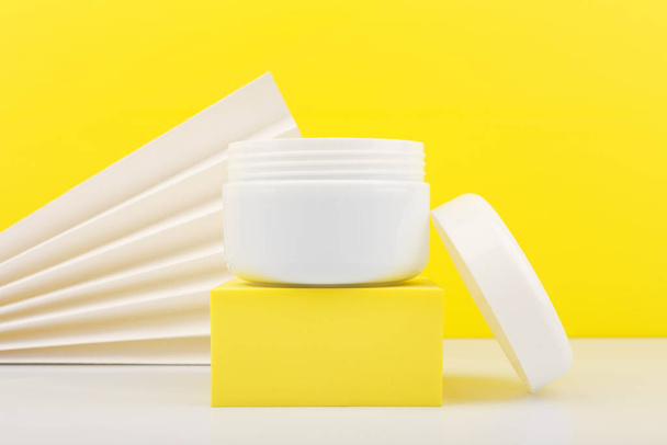 Close up of white opened jar on white table against yellow background decorated with white waver - Fotoğraf, Görsel