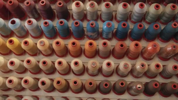 Bovenaanzicht van rijen draden voor het naaien in verschillende kleuren en tinten op een rek in een productiewerkplaats of atelier - Video