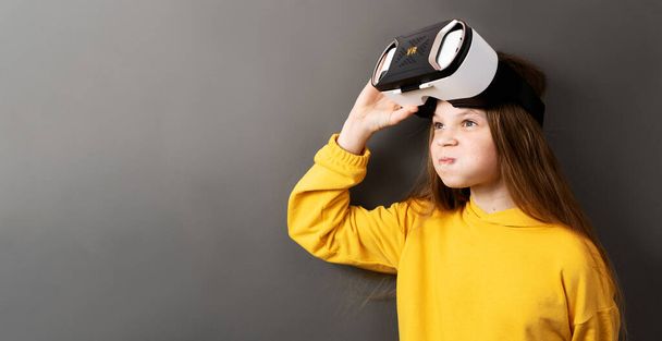 Enthusiastic little girl wearing virtual reality headset modern innovation device isolated on gray studio background. Female kid playing vr game in electronic helmet enjoying futuristic immersion - Fotoğraf, Görsel