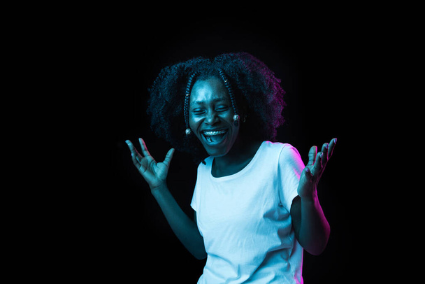 Young beautiful African-American girl isolated on dark background in neon light - Zdjęcie, obraz