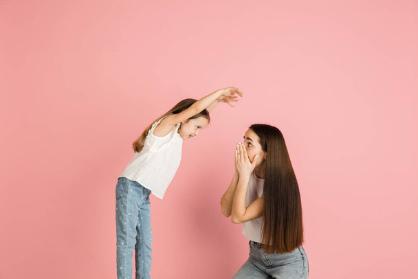Young woman and girl, mother and daughter isolated over pink background. - Foto, Bild