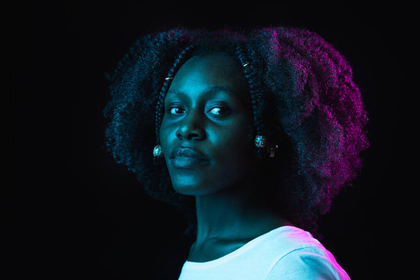 Jovem bela menina afro-americana isolada no fundo escuro em luz de néon - Foto, Imagem