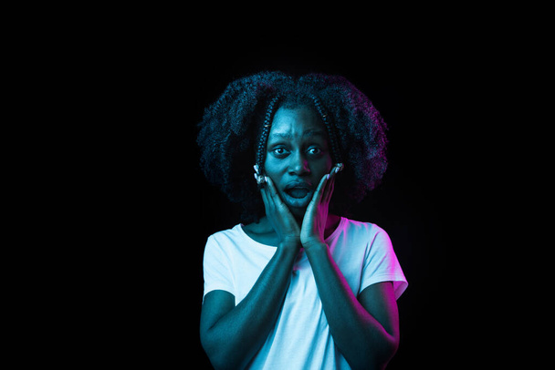 Νεαρή όμορφη Αφρο-Αμερικανίδα κοπέλα απομονωμένη σε σκούρο φόντο σε νέον φως - Φωτογραφία, εικόνα