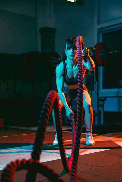 Молодая спортсменка, инструктор по фитнесу в спортзале в смешанном неоновом свете. - Фото, изображение