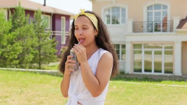 Retrato medio de una hermosa joven con el pelo largo y rizado bebiendo limonada refrescante al aire libre en el caluroso día de verano sonriendo a la cámara - Metraje, vídeo