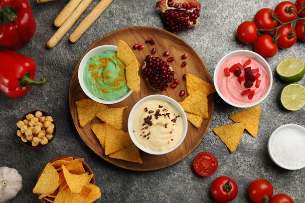Different kinds of tasty hummus served with nachos on grey table, flat lay - Fotografie, Obrázek