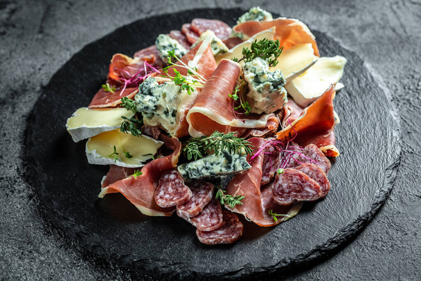 Antipasto board with sliced meat, ham, salami, cheese for red wine. Traditional Spanish meat snacks on a slate board. - Photo, Image