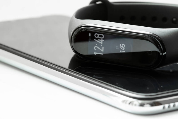 Schwarze Fitness-Uhr oder Aktivitätstracker mit Zeit- und Schrittanzeige. Fitness-Tracker liegt auf den Smartphones. Nahaufnahme, selektiver Fokus - Foto, Bild