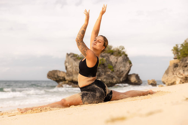 Práctica de yoga. Hermosa mujer caucásica practicando Hanumanasana, Monkey Pose o Front Split. Levanten los brazos. Los isquiotibiales se estiran. Retiro de yoga. Playa de Thomas, Bali, Indonesia - Foto, imagen