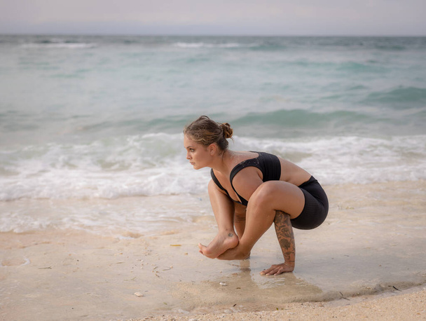 Ourdoor yoga. Attractive woman practicing Bhujapidasana, Arm Pressure Balance on the beach. Strong healthy body. Healthy lifestyle. Yoga retreat. Copy space. Thomas beach, Bali, Indonesia - Photo, Image