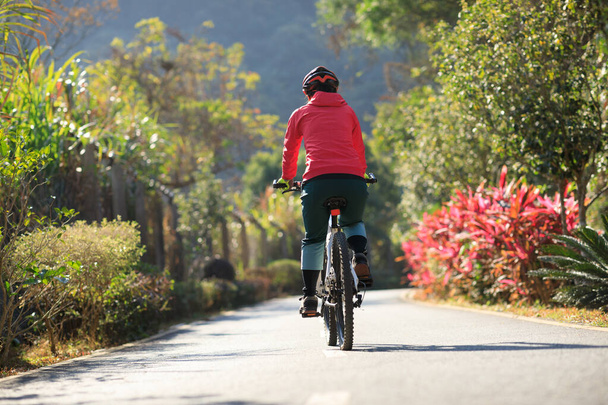 Woman riding a bike on tropical park trail in spring - Foto, Bild