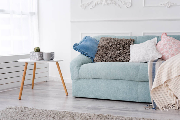 Μοντέρνο ξύλινο τραπεζάκι σαλονιού και άνετος καναπές με μαξιλάρια. Σαλόνι εσωτερικό και απλή μοντέρνα διακόσμηση έννοια - Φωτογραφία, εικόνα