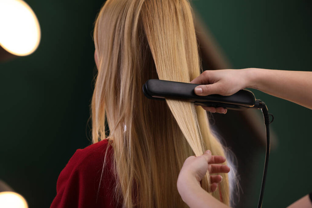 Stylist straightening woman's hair with flat iron in salon - Foto, Imagen